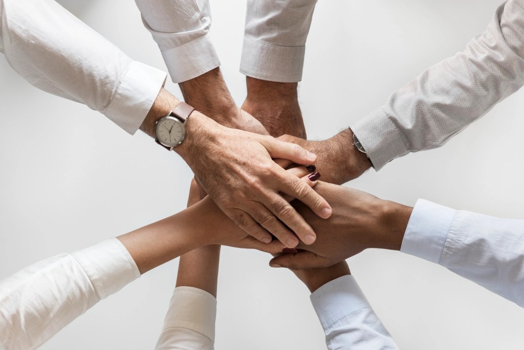 A group of diverse hands overlapping in a team huddle, symbolizing teamwork and collaboration.
