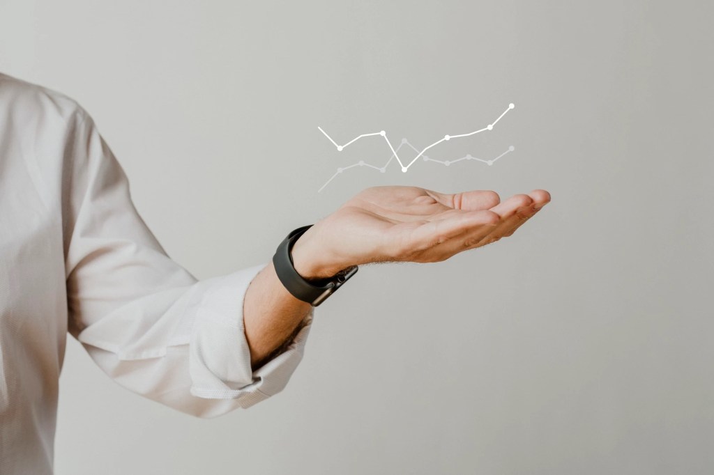 A person in a white shirt holds out their palm, with a graphical representation of fluctuating data lines displayed above it.
